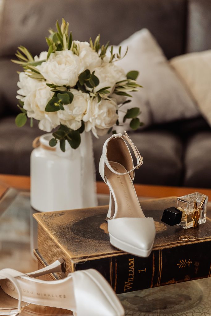 Zapato de tacón, ramo, perfume y libro antiguo en bodegón.